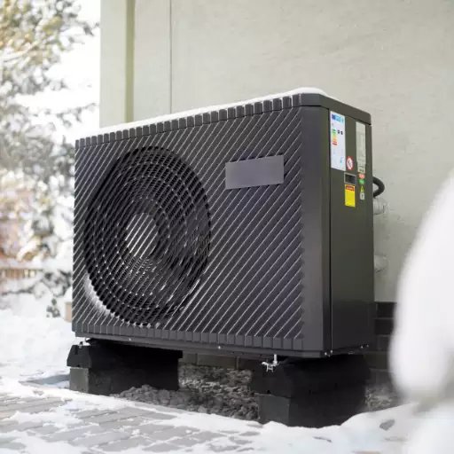 A cold weather heat pump in the snow outside of a house.